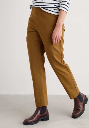 Bruine, rechte broek van een textuurstof, met zijzakken en een enkele knoopsluiting. Gepaard met donkerbruine enkellaarsjes.