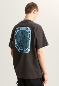 Donkergrijze t-shirt met een relaxte pasvorm, voorzien van een blauwe graphic op de achterkant met de tekst "HEAVY THINKER" en een illustratie van een spinnenweb.