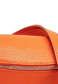 Oranje leren tas met textuur, voorzien van een ritssluiting en een bijpassende schouderriem. Het oppervlak heeft een gegranuleerde afwerking met een strakke, moderne uitstraling.