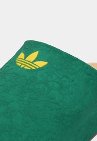 Zöld velúr papucs, dombornyomott virágmintával és elöl sárga hímzett háromcsíkkal díszítve.