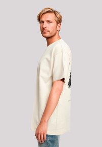 Beige cotton T-shirt with short sleeves, featuring a black tree graphic on the back, crew neckline, and relaxed fit.