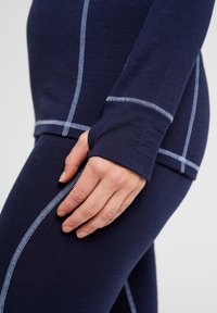 Marineblå langærmet top med kontrasterende lyseblå syninger, tætsiddende design og tommelhuller; parret med matchende strækleggings.
