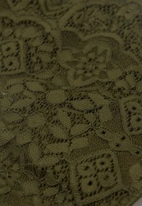 Tissu en dentelle vert olive présentant des motifs floraux et géométriques complexes, avec une variété de textures et d'ouvertures tout au long.