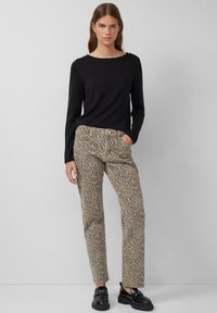 Top a maniche lunghe nero abbinato a pantaloni a fantasia leopardata in toni beige e marrone. Il modello indossa scarpe nere con suola spessa.