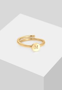 Anello d'oro con una fascia sottile e un disco circolare con una "M" in rilievo, che mette in mostra un design minimalista e una superficie liscia.