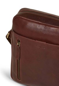 Borsa a tracolla in pelle marrone con finitura testurizzata, dotata di una tasca con zip sul davanti e branding impressato, forma rettangolare.