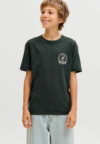 Tamsiai žalia trumpomis rankovėmis marškinėliai, pagaminti iš medvilnės, su apvaliu balto grafikos dizainu kairėje krūtinės pusėje ir klasikiniu apykaklės iškirpimu.