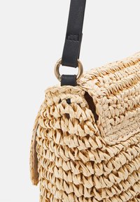 Woven straw handbag v přirozené barvě s texturovaným povrchem, vybavená černým koženým popruhem a kulatým kovovým akcentem.