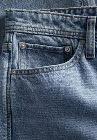Jeans de denim azul con un diseño clásico de cinco bolsillos, que cuentan con costuras naranjas en contraste y detalles en metal plateado en los bolsillos.