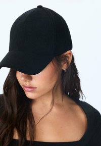 Crna korduroy bejzbol kapa s zakrivljenim šiltom, glatke teksture, dizajna s šest panela i detaljem gumba na vrhu.