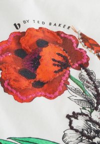 Geborduurd bloemenpatch op witte stof met levendige rode en zwarte bloemdetails, omringd door groene bladeren, met kleurenrijk garen.