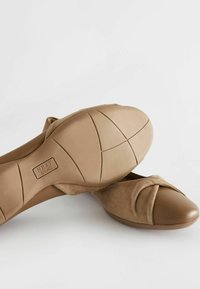 Beige slip-on kengät, joissa on pehmeä mokkanahka yläosa ja pyöreä kärki, varustettu solmitulla muotoilulla ja sileällä kumipohjalla.