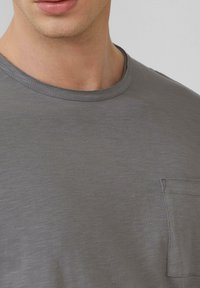 Szara krótka koszulka z krótkim rękawem wykonana z miękkiego materiału. Posiada okrągły dekolt oraz małą kieszonkę po lewej stronie klatki piersiowej. Widoczna subtelna tekstura.