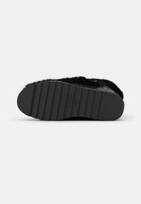 Zapatilla negra con textura de piel, suela exterior de goma con ranuras horizontales y detalle de logo en relieve en la suela.