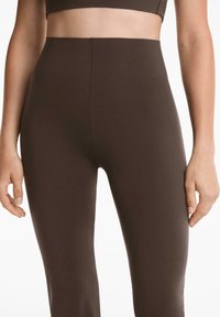 Leggings marron taille haute en tissu lisse et extensible, avec un design sans coutures, arborant une taille légèrement texturée.