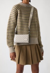 Krémová kabelka s geometrickým vzorem, nastavitelné ramínko a stříbrné doplňky, v kombinaci s pruhovaným svetrem a plisovanou sukní.