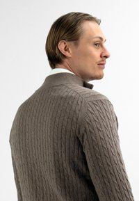 Bruine gebreide cardigan met kabelpatroon, met een hoge kraag en ribbeltextuur, weergegeven vanuit een driekwart achteraanzicht.