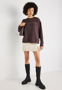 Sweatshirt castanho com o texto "Dolce Far Niente", saia mini canelada creme com fendas laterais e botas pretas até ao joelho.
