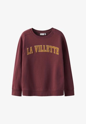 Burgundski pulover z okroglo ovratnikom, ribastimi manšetami in robom. Na sprednji strani je v zlatem vezenem besedilu napisano "LA VILLETTE".