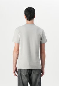 Γκρίζο βαμβακερό μπλουζάκι με κοντά μανίκια και στρογγυλή λαιμόκοψη, εμφανιζόμενο από πίσω. Συνδυάστε με σκούρο γκρίζο τζιν.