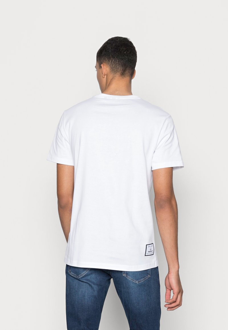 T-shirt en coton blanc à manches courtes, col rond, avec un détail d'étiquette à l'ourlet. Texture lisse, coupe décontractée.
