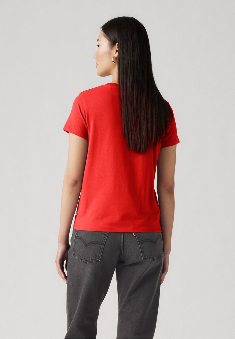 Camiseta corta roja de algodón con cuello redondo. Combinada con unos vaqueros gris de cintura alta con detalles de costura en los bolsillos traseros.