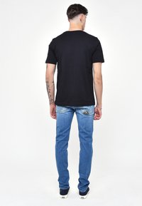 T-shirt corto nero abbinato a jeans in denim azzurro chiaro. I jeans presentano un design distintivo della tasca posteriore. Sono indossate scarpe casual.