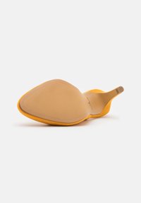 Žlutá vysoká botka na podpatku s hladkým, zaobleným špičkou a stiletto podpatkem. Podešev je béžová a má texturovaný svršek připomínající semiš.