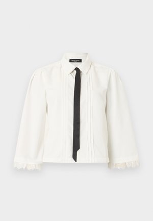 Blouse blanche à manches longues avec des plis, des poignets en dentelle, une cravate noire fine et un col pointu sur un fond uni.
