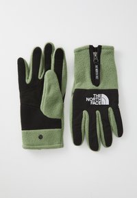 Két kesztyű, az egyik zöld fleece, a másik fekete szintetikus tenyérrel, cipzárral, textúrázott fogással és logó részletekkel. Puha, meleg anyag.