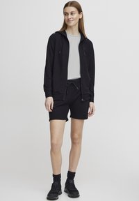 Black zip-up hoodie with drawstring, paired with black shorts. Smooth fabric, minimalistic design, features side pockets and elastic waistband.