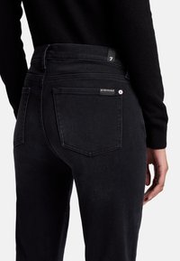 Jeans in denim nero con vita alta, due tasche posteriori e cuciture discrete. Presenta un'etichetta in vita e una superficie liscia e morbida.