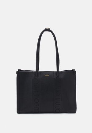 Sac fourre-tout rectangulaire noir avec de longues anses et de discrètes rayures verticales embossées, avec un petit logo de marque doré au centre.