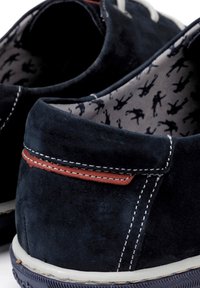 Chaussures en suède bleu marine avec un contraste de coutures rouges et une semelle blanche. L'intérieur est doté d'une doublure grise à motifs avec de petites figures noires.