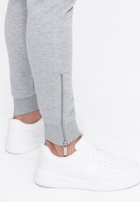 Gray sweatpants with a side zipper detail, paired with white sneakers featuring a textured upper and thick sole.