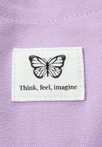 Tissu violet avec une étiquette blanche présentant une illustration de papillon noir et le texte "Pensez, ressentez, imaginez" en dessous.