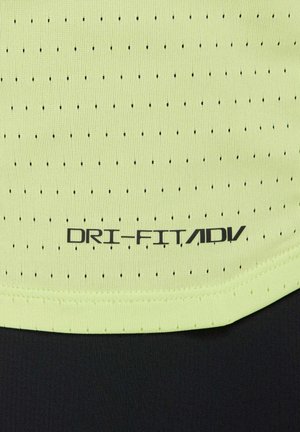 Tissu texturé vert clair avec de petites perforations noires. L'étiquette indique "DRI-FIT/ADV" en noir. Présente une bande noire en bas.