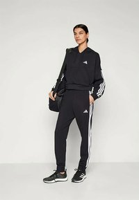 Completo sportivo nero composto da una felpa con zip e pantaloni affusolati, con strisce bianche lungo le maniche e i lati.