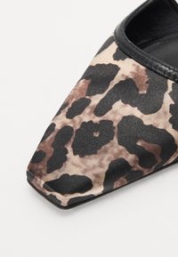 Chaussure à bout pointu avec un dessus en tissu imprimé léopard noir et beige, présentant un revêtement en cuir noir lisse le long de l'ouverture et une surface texturée.