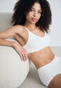 Bijela bešavna bralette i odgovarajuće kratke hlače viskog struka. Mekani materijal, elegantan dizajn, minimalistički oblik, bez vidljivih hardverskih detalja ili uzoraka.