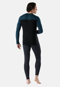Long-sleeve athletic top in teal and black, paired with dark gray fitted leggings. Soft, stretchy fabric with a smooth texture.