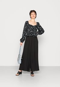 Blusa preta de manga longa com bolinhas azuis claras, combinada com calças pregueadas pretas de cintura alta e sandálias pretas de salto bloco. Bolsa azul clara.