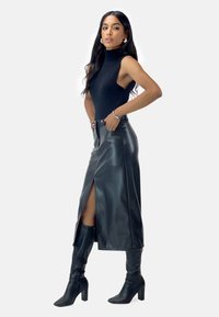 Cuello alto sin mangas negro, falda de cuero de talle alto con una abertura en el frente y botas negras hasta la rodilla con tacón. Textura lisa en toda la prenda.