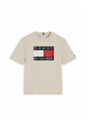 Beżowy T-shirt z krótkim rękawem z logo Tommy Hilfiger, na którym znajduje się czerwono-biało-czarna prostokątna flaga oraz nazwa marki z przodu.