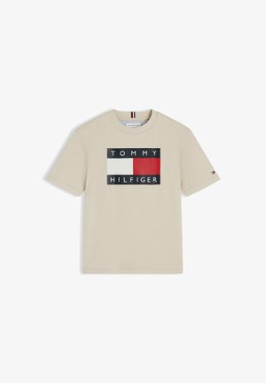 Beige T-shirt met korte mouwen met het Tommy Hilfiger-logo, met een rood, wit en zwart rechthoekig vlaggetje en merknaam aan de voorkant.