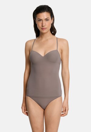 Donna in piedi, rivolta in avanti, che indossa una canottiera senza cuciture color taupe e biancheria intima abbinata, su uno sfondo chiaro e uniforme.