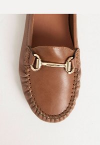 Brauner Lederloafer mit gestickten Details und einem goldfarbenen Metallakzent. Glatte Oberfläche, abgerundete Form und Schlupfdesign.