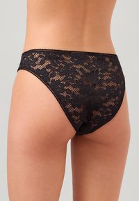 Svarta högmidjade bikiniunderdelar i spets med blommönster, genomskinlig textur och vågiga kanter, som erbjuder täckning och intrikata detaljer.