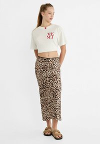 Skraćeni bijeli majica s natpisom "THE MET" u crvenoj boji, uparen s dugom suknjom s leopard uzorkom i smešnim sandalama. Glatka tkanina, opušteni kroj.