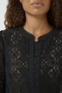 Blusa di pizzo nero con motivi floreali, scollatura rotonda con bordi scallop e piccoli bottoni lungo la parte anteriore.